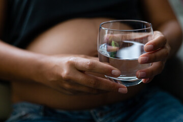 Pregnant woman holding a glass of water, body hydration, drinking plenty of fluids, healthy pregnancy