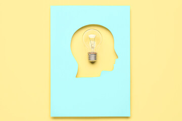 Light bulb visible through cut blue paper in shape of human head on yellow background