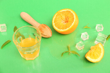 Orange with juicer, glass, ice cubes and mint on green background