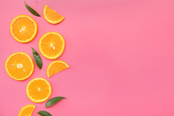 Orange slices with plant leaves and water drops on pink background