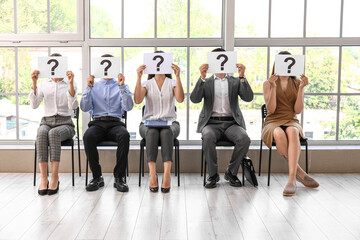 Young people holding paper sheets with question marks while waiting for job interview in office