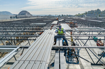 construction worker sitting on the roof of a warehouse welding