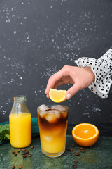 Woman preparing tasty orange espresso on grunge background