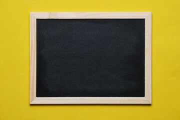 Fototapeta premium Black blackboard for notes in wooden frame yellow background.