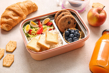 Lunchboxes with delicious food and bottle of juice on light background