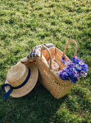 Picnic basket with blanket with straw hat and flowers bouquet on green grass in the park