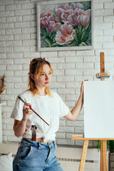 The artist paints in oils at the easel. In the hands of a palette and brush. White T-shirt and apron. Portrait. Creative person concept. 
