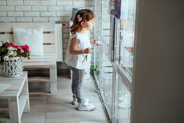 A child looks out the window. The girl is waiting for her mother to return from work