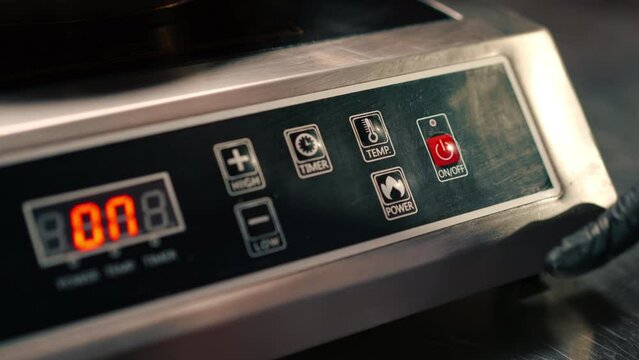 close-up of the chef's finger pressing the button to turn on the induction stove in a professional kitchen