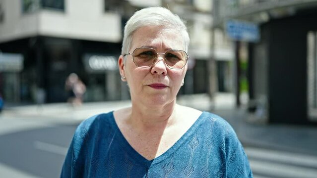 Middle age grey-haired woman standing with serious expression saying no with head at street