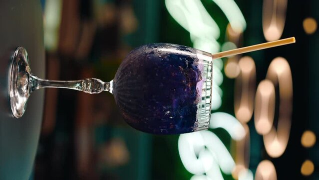 vertical video freshly prepared purple alcoholic cocktail rotates on the bar counter in the bar club