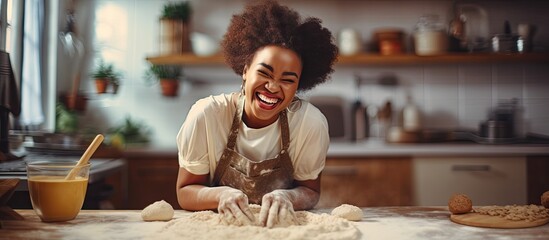 African woman enjoying herself in kitchen making dough - obrazy, fototapety, plakaty