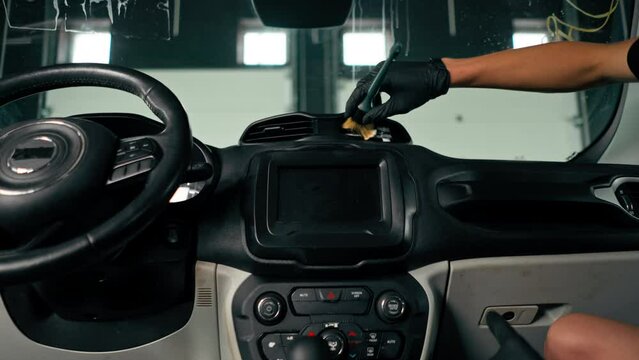 A close-up of a car wash worker using a brush and car chemicals to clean the dashboard of a luxury car during the detailing process