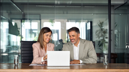 Professional business executive managers office team working using laptop computer sitting at table. Two middle aged colleagues company board discussing digital strategy at corporate meeting.