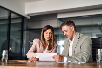 Two professional executives discussing financial accounting papers working together in office. Mature business woman manager consulting older man client holding legal documents at meeting.