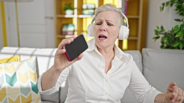 Middle age grey-haired woman listening to music singing song at home
