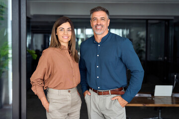 Smiling Latin middle aged business man and woman in office, portrait. Two happy confident...