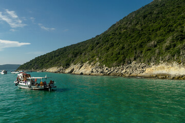 Formação rochosa a beira-ma com muita vegetação, céu azul e pequena embarcação no mar, localizada na região de Cabo Frio, Rio de Janeiro, Brasil - 30