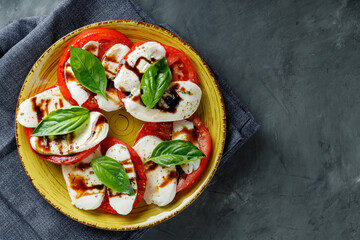 Salad Caprese with tomato, mozzarella and fresh basil on dark background. Top view. Copy space