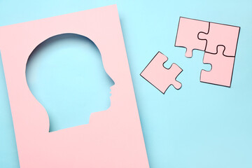 Cut pink paper in shape of human head with puzzle pieces on blue background. Logic concept