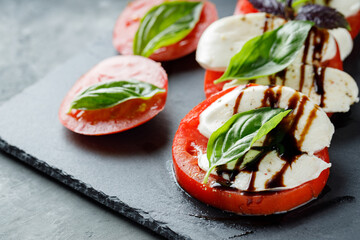 Italian Caprese Salad with sliced tomatoes, mozzarella and basil on slate board. Close up