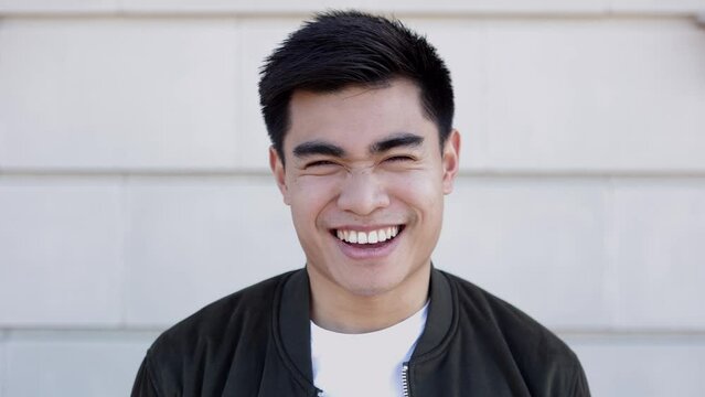 Portrait of young asian man smiling at camera standing over outdoors background. Front view headshot of happy millennial filipino guy.