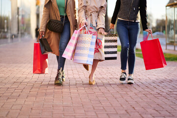 Cropped image of three unrecognizable modern women walking down street of city and carrying...