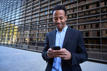Young adult Latin professional outside modern office building using phone. Business man in formal...