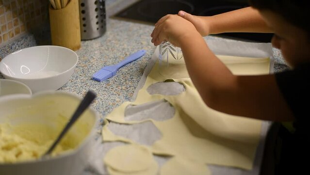 Children's hands make circles of thin puff pastry for cottage cheese buns using a glass
