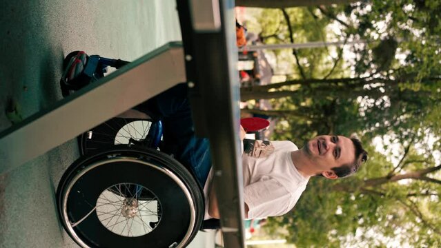 vertical video A man in a wheelchair plays table tennis in a city park emotionally practices his shots with a ping pong racket