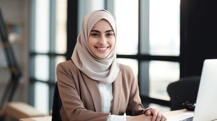 Attractive middle eastern businesswoman woman posing at her work place sitting at her desk using a computer - obrazy, fototapety, plakaty