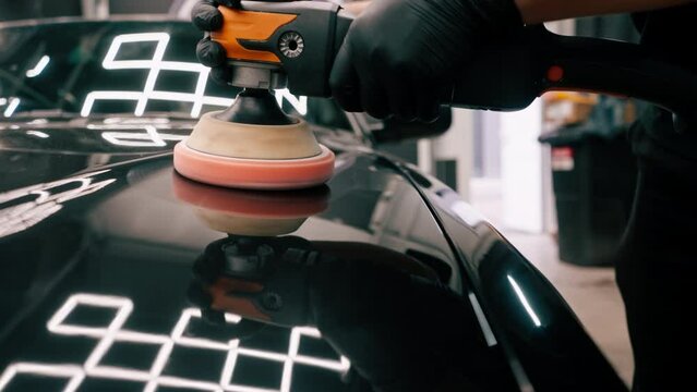 Close-up of a car wash worker using a polishing machine to polish the hood of  black luxury car