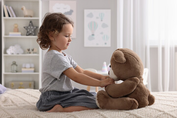 Cute little girl playing with teddy bear on bed at home