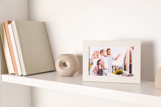 Photo frame with family portrait and books on white shelf indoors