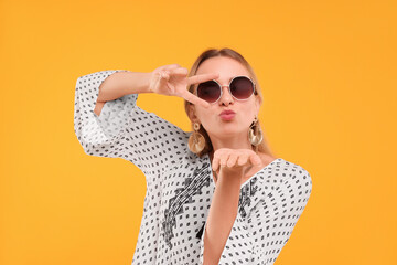Portrait of beautiful hippie woman showing peace gesture and blowing kiss on yellow background