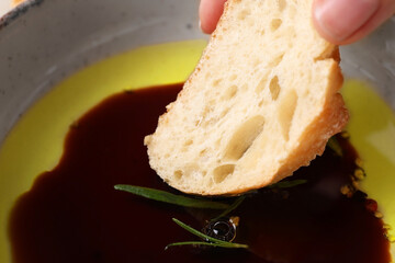 Woman dipping piece of bread into balsamic vinegar with oil and rosemary in bowl closeup