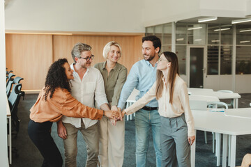 Team of smiling business colleague holding hands together in a huddle standing in a modern office....