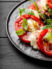 Delicious caprese salad with ripe tomatoes, mozzarella cheese and fresh basil leaves on dark wooden boards. Close up