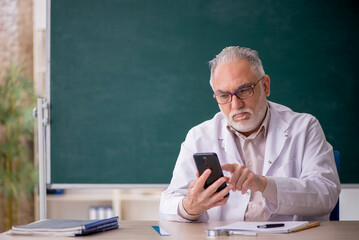 Old male teacher in front of green board