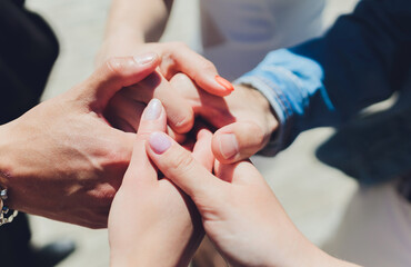 two man and three women holding hands on a table implying a polyamory relationship or love triangle.