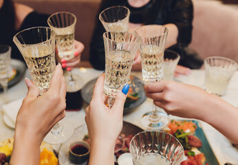 Close up shot of group of people clinking glasses with wine or champagne in front of bokeh...