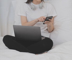 Efficient Young Millennial Girl Sitting on a Bed in the Morning, Uses Laptop Computer and Eats Croissants and Drinks Coffee for Breakfast