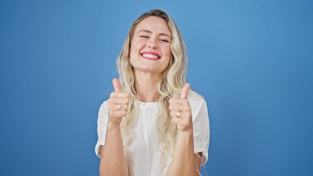 Young blonde woman smiling with thumbs up over isolated blue background