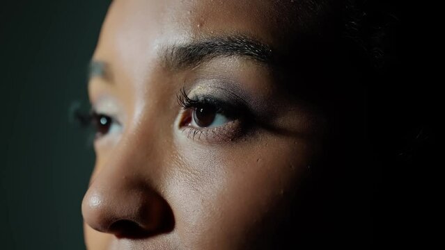 Young African woman opening eyes in dark room.
