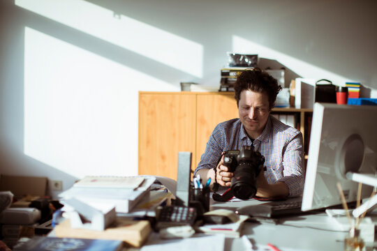 Young photographer going through his camera at his desk office
