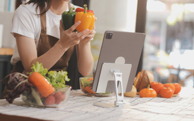 Delicious fruit and vegetables on a table and woman cooking. Housewife is cutting green cucumbers on a wooden board for making fresh salad in the kitchen.