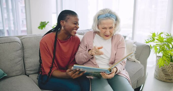 Photo album, assisted living and a senior laughing with her black woman caregiver on a sofa in the living room. Smile, funny and elderly resident looking at a memory with a nurse in a retirement home