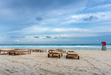 Fototapeta na wymiar Afternoon with empty lounge chairs on empty beach at Zona Hotelera (Hotel Zone) on a cloudy day in Cancun, Mexico
