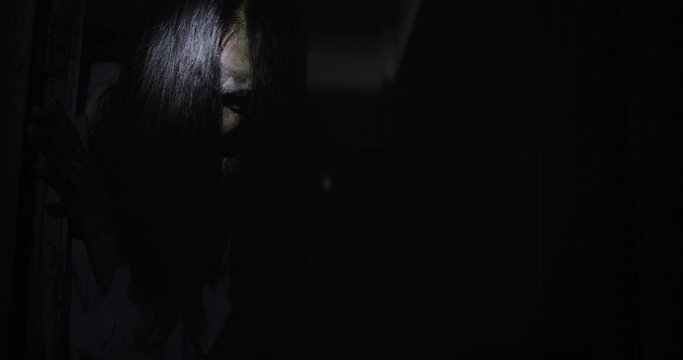 Horror scene of a mysterious Scary Asian ghost woman creepy have hair covering the face looking to camera with flashlight in restroom and dark scene movie at night, holiday Halloween ghost concept