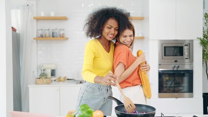 Happy young woman friends enjoy singing and dancing while cooking at kitchen room. Lesbian couple having fun singing dancing together while cooking together at home